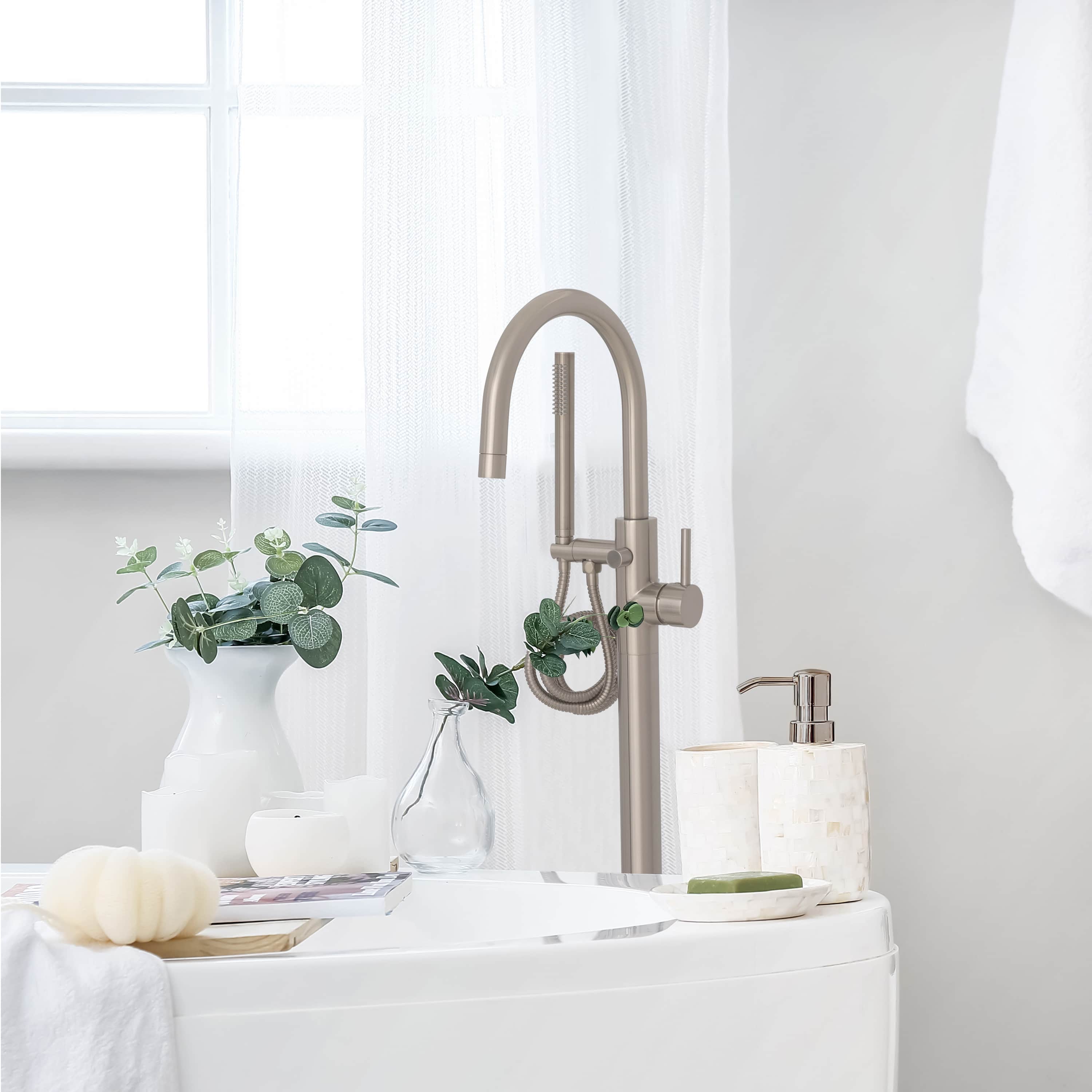 Brushed nickel bathtub filler faucet with curved spout and hand shower hose on tub deck.