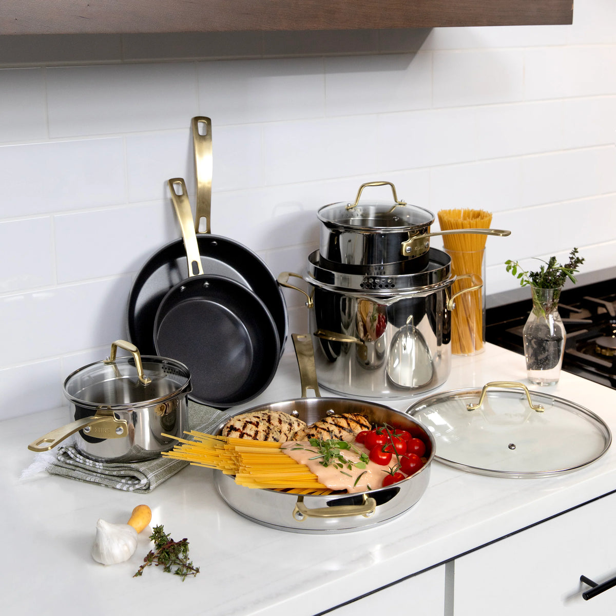Stainless steel cookware set with nonstick pans, pots, and lids on a kitchen countertop