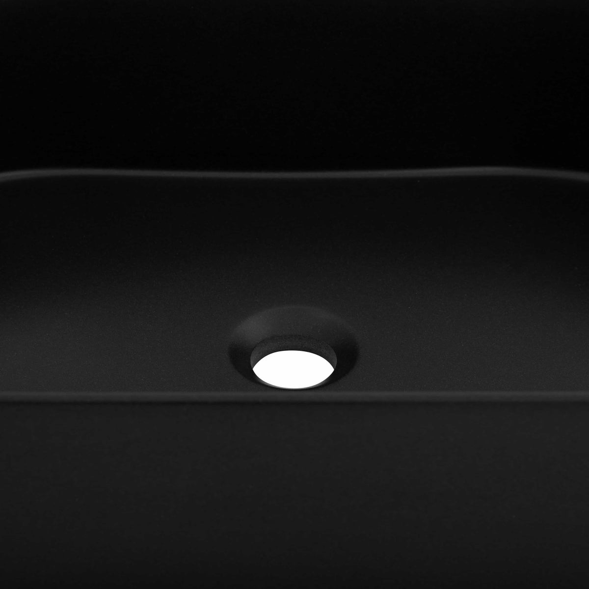 Close-up of round drain hole in matte black oval vessel sink