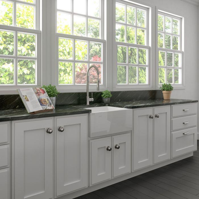 White farmhouse apron-front single-bowl sink in a bright kitchen with cabinet base