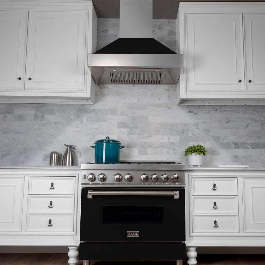 Wall-mounted range hood with black matte canopy above stainless vent grille in white kitchen.