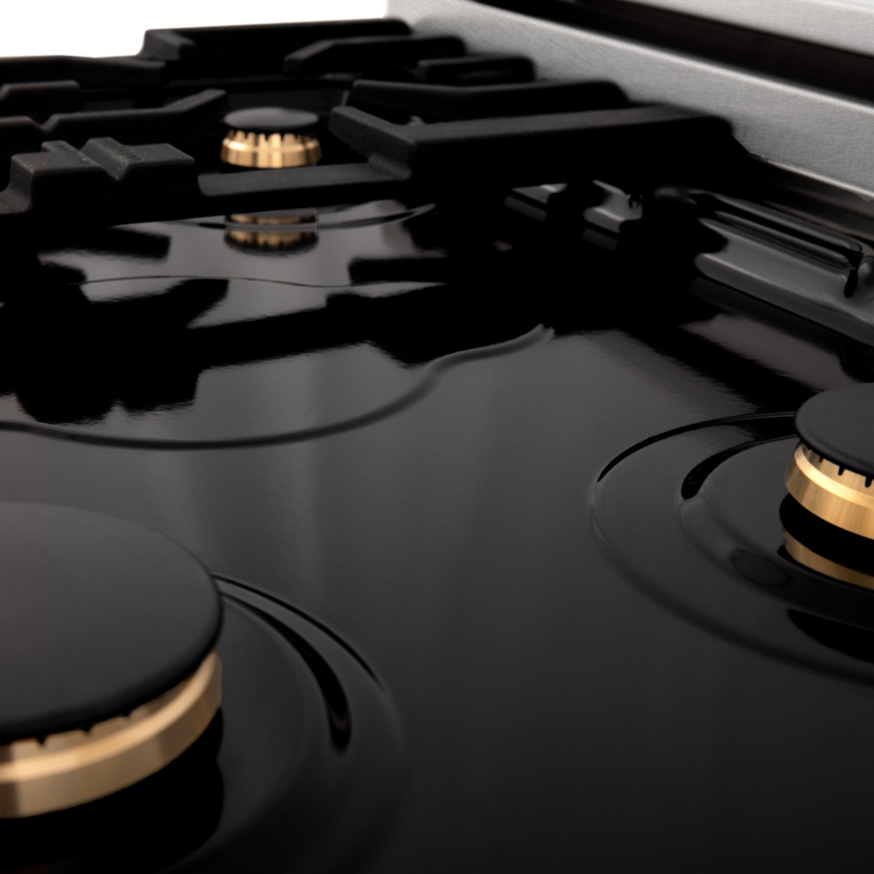 Black cooktop with round burner heads and brass accents on a satin stainless range