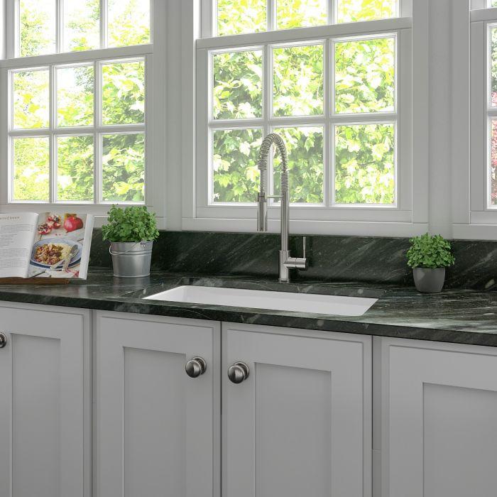 White fireclay single-bowl sink installed under window with faucet and drain opening