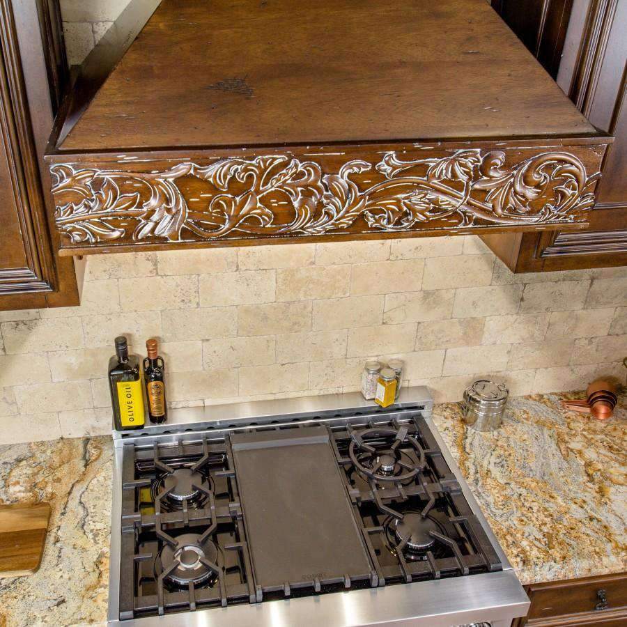 Wooden wall range hood above a stainless cooktop with ornate carved trim