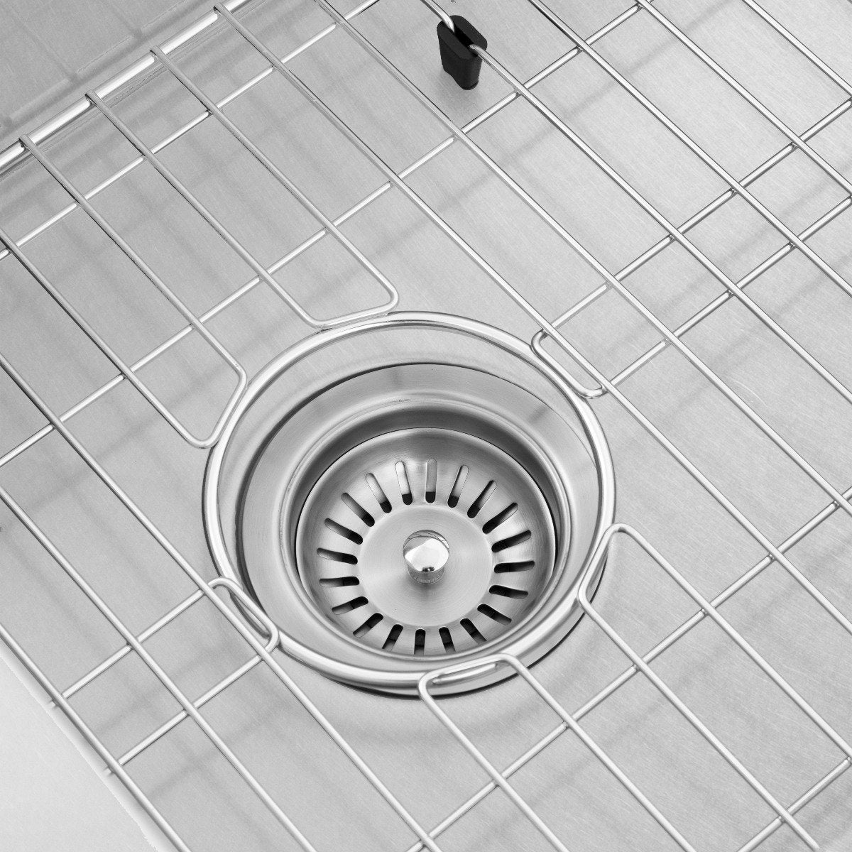 Round stainless drain strainer centered on a wire bottom grid in a sink basin