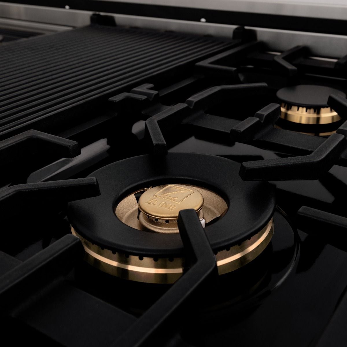 Brass burner cap on black cooktop grate with pan supports and burner ring