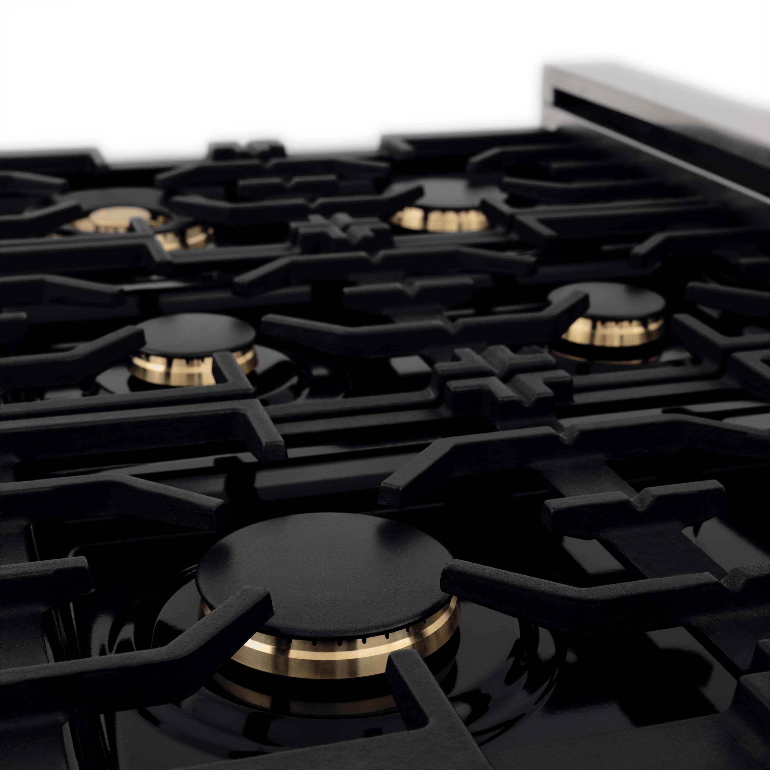 Black gas burner grates with brass flame caps on stainless cooktop