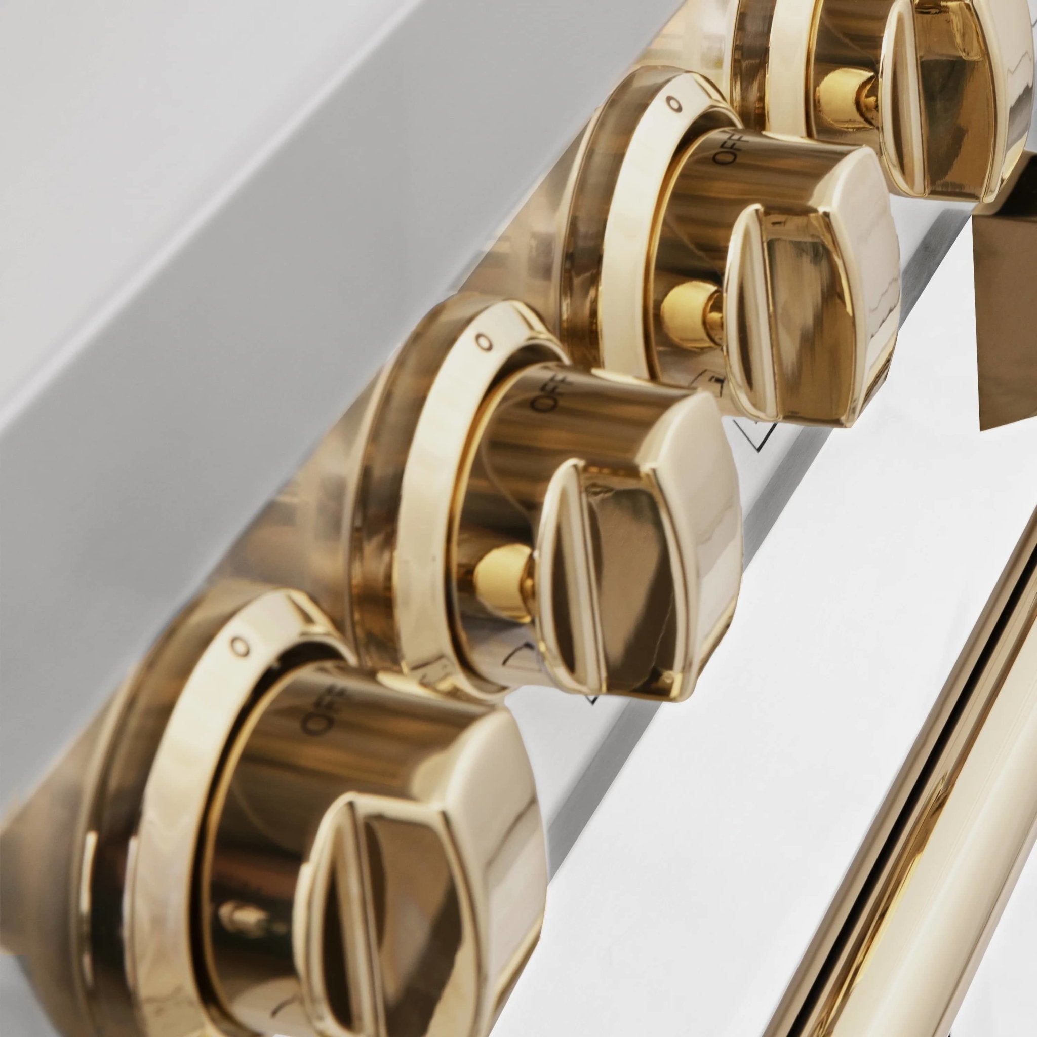 Gold control knobs on a white range cooktop panel