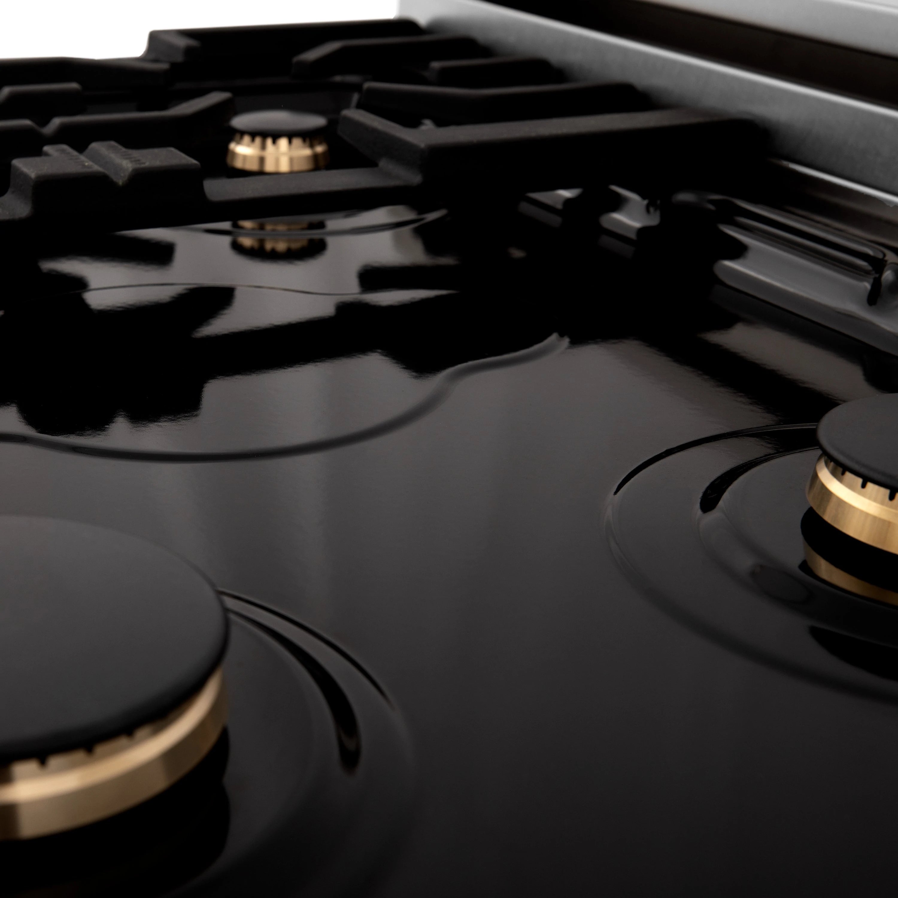 Close-up of black cooktop burners with gold center rings and control knobs