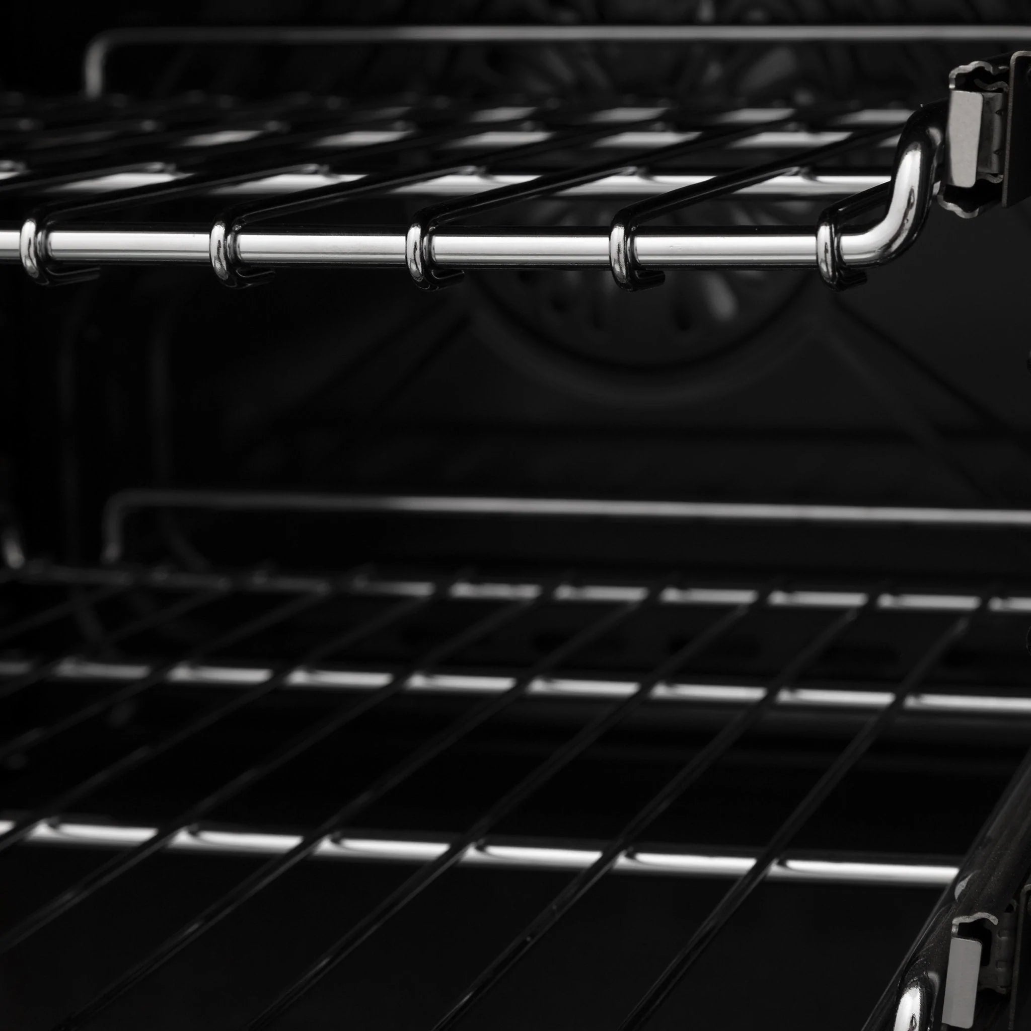 Black oven cavity with wire racks and chrome cooktop supports, close-up