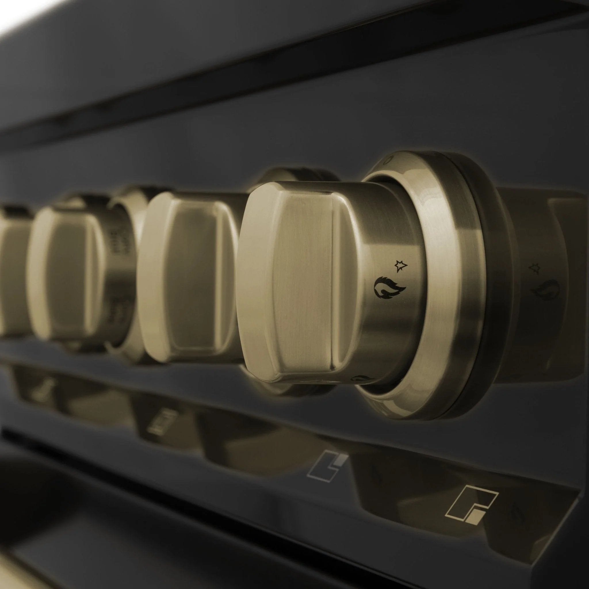 Close-up of champagne bronze knobs and icons on a black range control panel