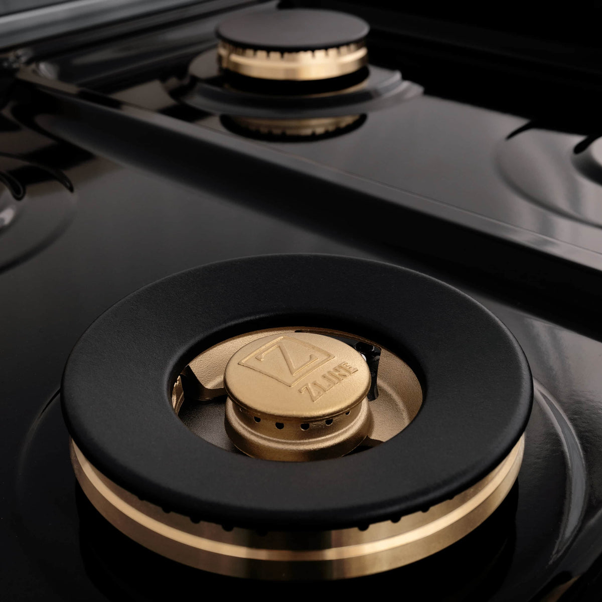 Black gas burner with brass cap on a matte black cooktop surface