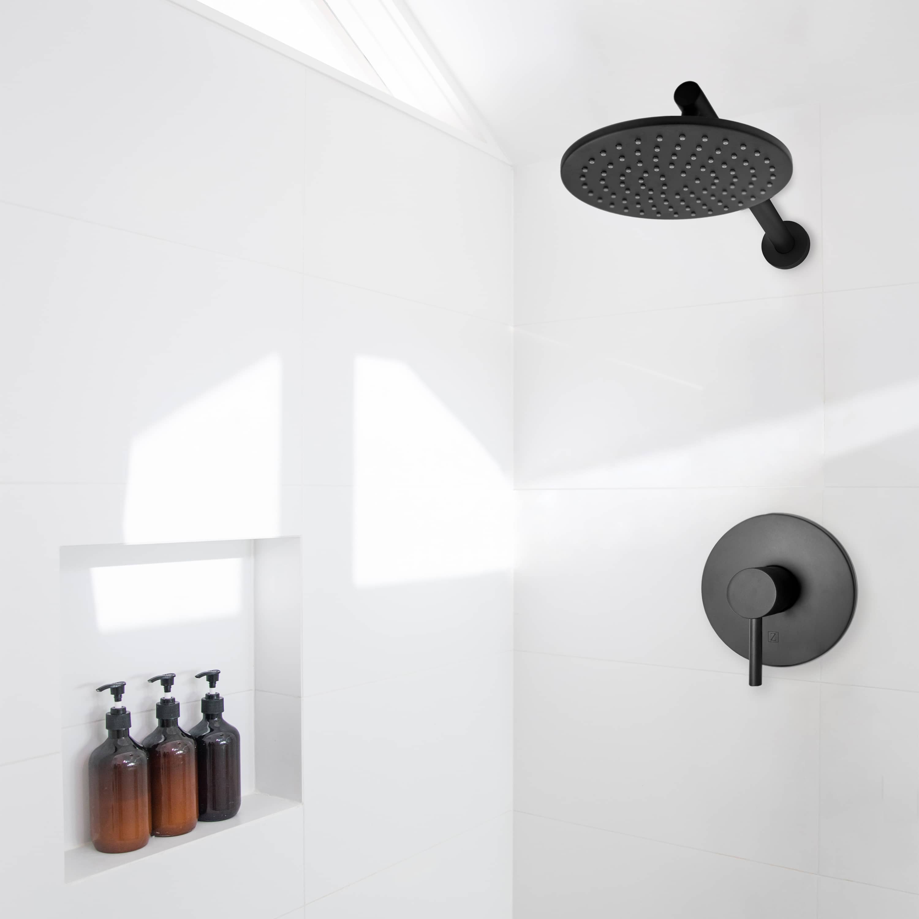 Matte black wall-mounted showerhead with round control handle on shower wall.