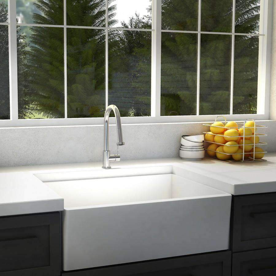 Chrome kitchen faucet with curved spout on white sink by a large window
